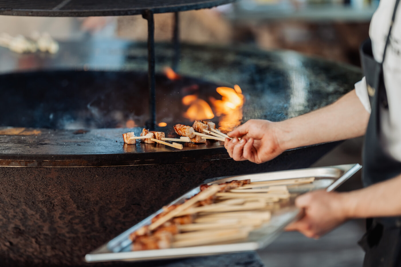 Kok grilt spiesjes boven open vuur op de ronde ijzeren grillplaat bij De Barrier