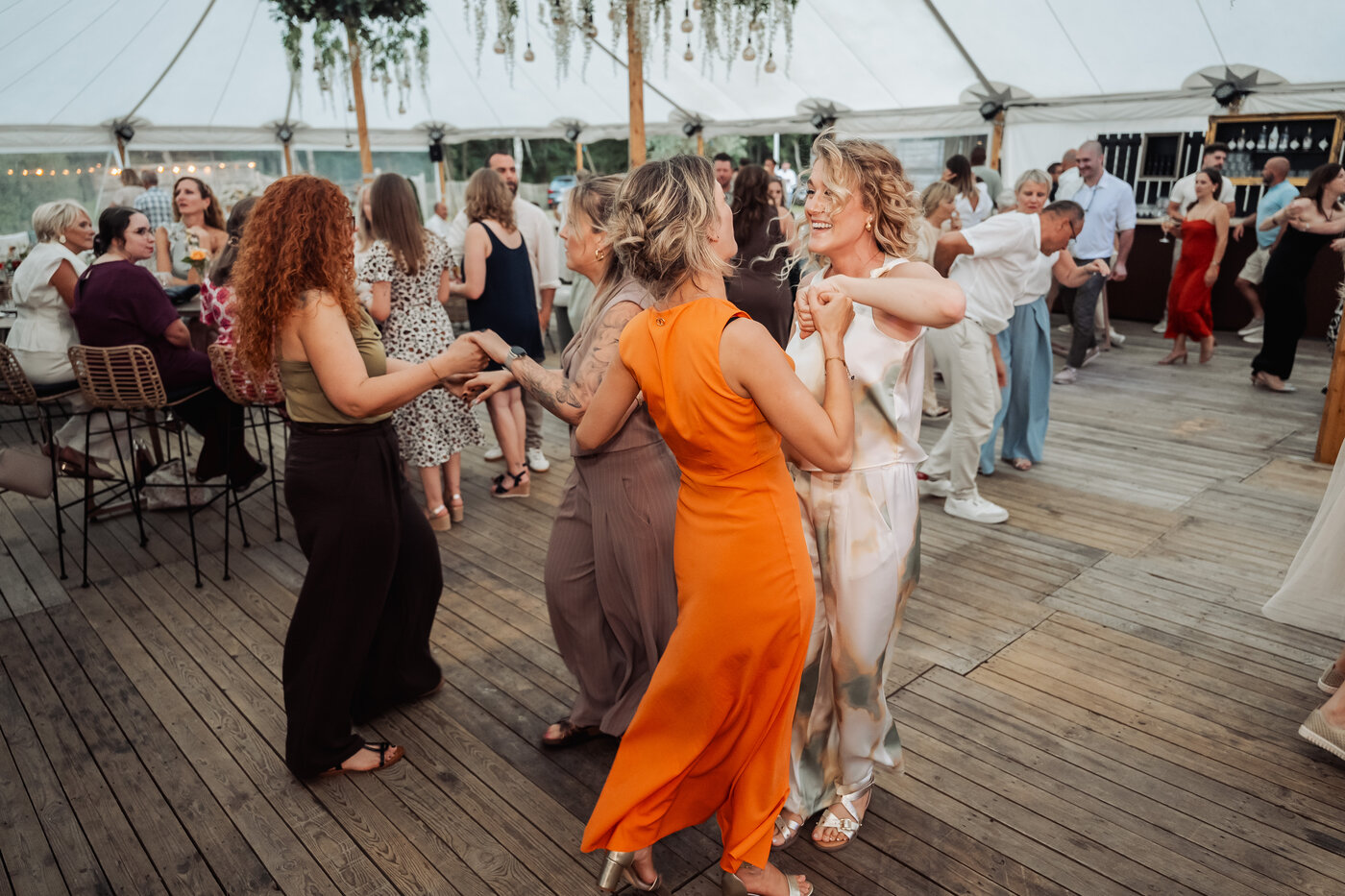 Gasten dansen uitgelaten op de houten dansvloer in de open stretch tent bij De Barrier, met de avondlucht zichtbaar door de open zijkanten