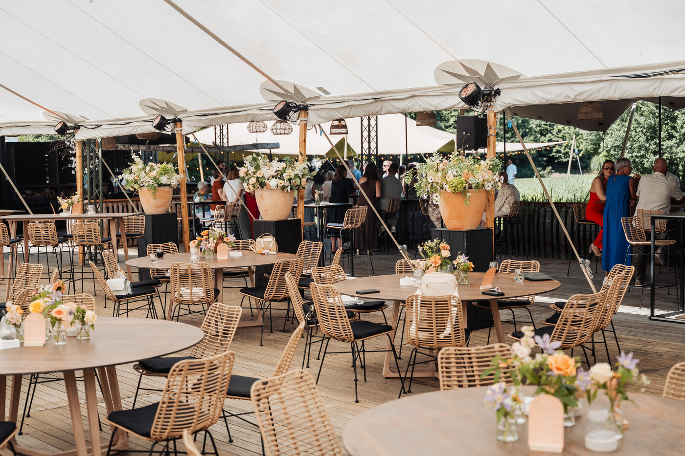 Interieur van de feesttent bij De Barrier met rotanstoelen, ronde tafels, bloemstukken en sfeerverlichting