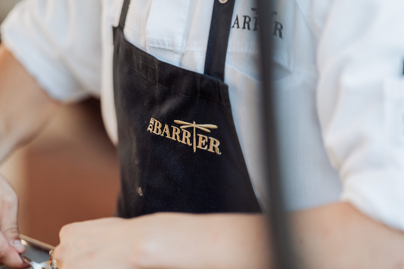 Zwart schort met het goudgeborduurd logo van De Barrier