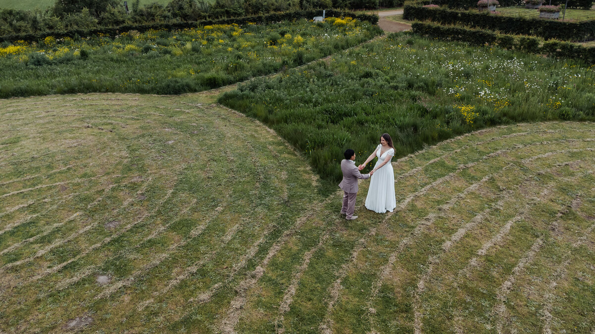 Bruidspaar Sofie en Jaya hand in hand op het landgoed bij Kasteel Limbricht, gefotografeerd vanuit de lucht
