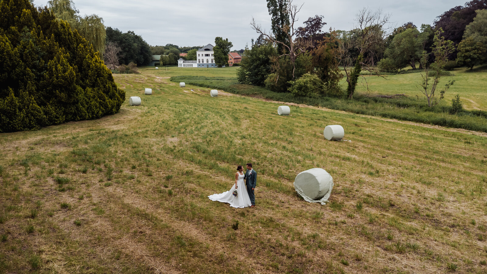 Luchtfoto van bruidspaar Bram en Elien in een zonnig veld met hooibalen nabij De Waerboom