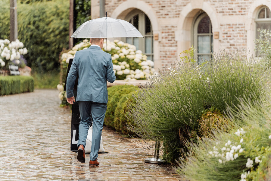 Bruidegom haast zich met een paraplu door de regen naar De Waerboom
